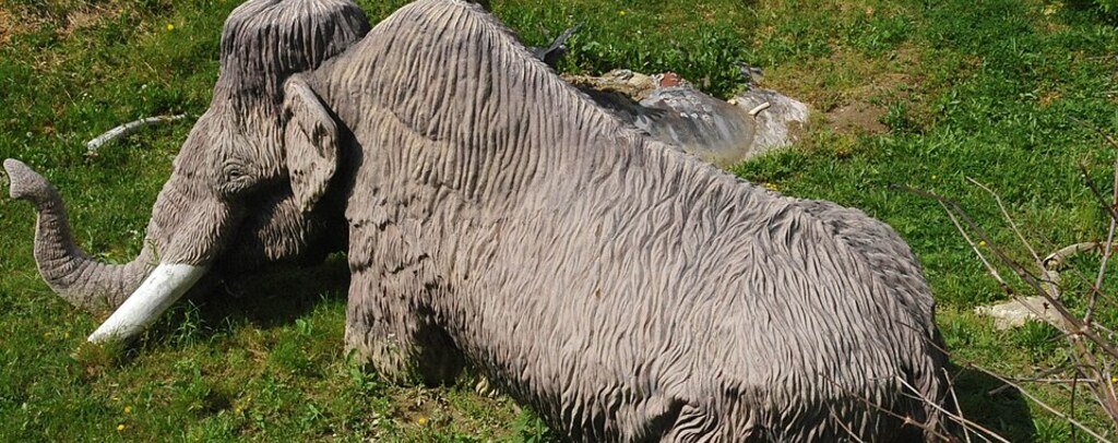 Life-size mammoth display appearing stuck in soft earth at Big Bone Lick State Historic Site in Kentucky