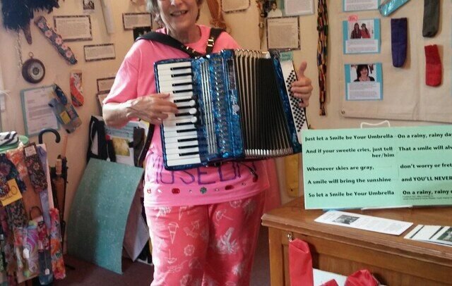 Nancy 3. Hoffman playing accordion among umbrella covers inside the Umbrella Cover Museum on Peaks Island