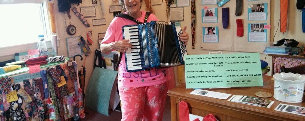 Nancy 3. Hoffman playing accordion among umbrella covers inside the Umbrella Cover Museum on Peaks Island